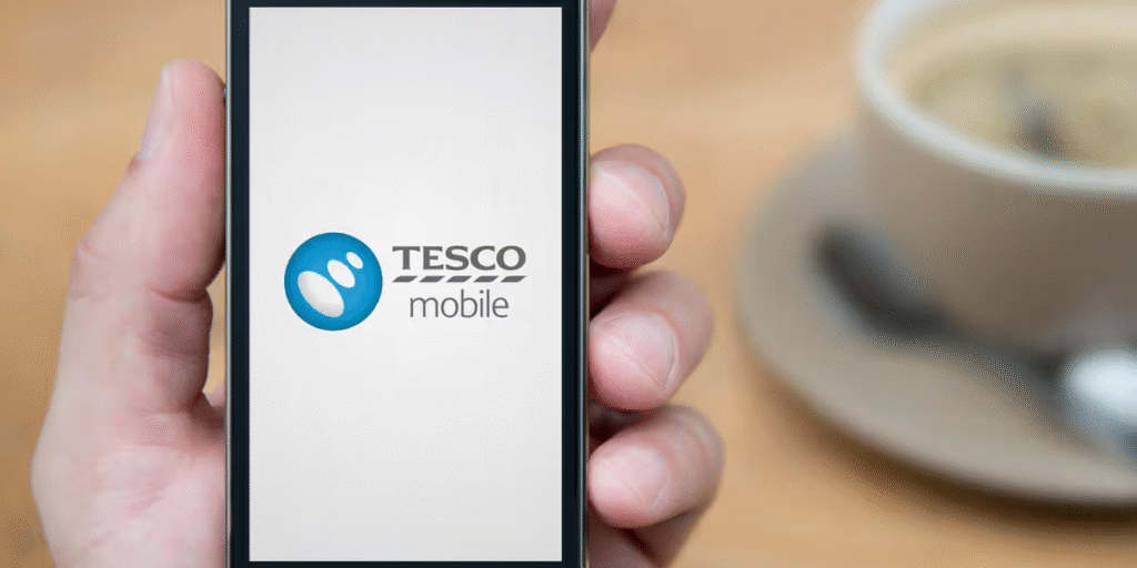 A person using a modern smartphone connected to the Tesco Mobile network while managing daily digital tasks such as video calling, online shopping, mobile banking, social media, and streaming. The image features a clean digital workspace with strong mobile connectivity, 5G technology, and a user-friendly mobile app, representing the convenience of today's connected lifestyle. It highlights how Tesco Mobile supports affordable, reliable communication for families, professionals, students, and travellers through flexible mobile plans and seamless digital experiences. The modern setting reflects smart connectivity, fast internet access, and everyday convenience, showcasing how mobile technology has become an essential part of work, entertainment, travel, and staying connected in 2026.